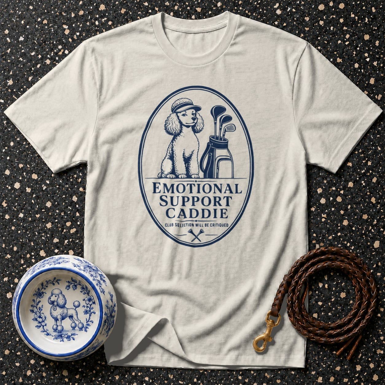 T-shirt with blue graphic of a poodle wearing a golf hat, golf bag, clubs, and text: Emotional Support Caddie.