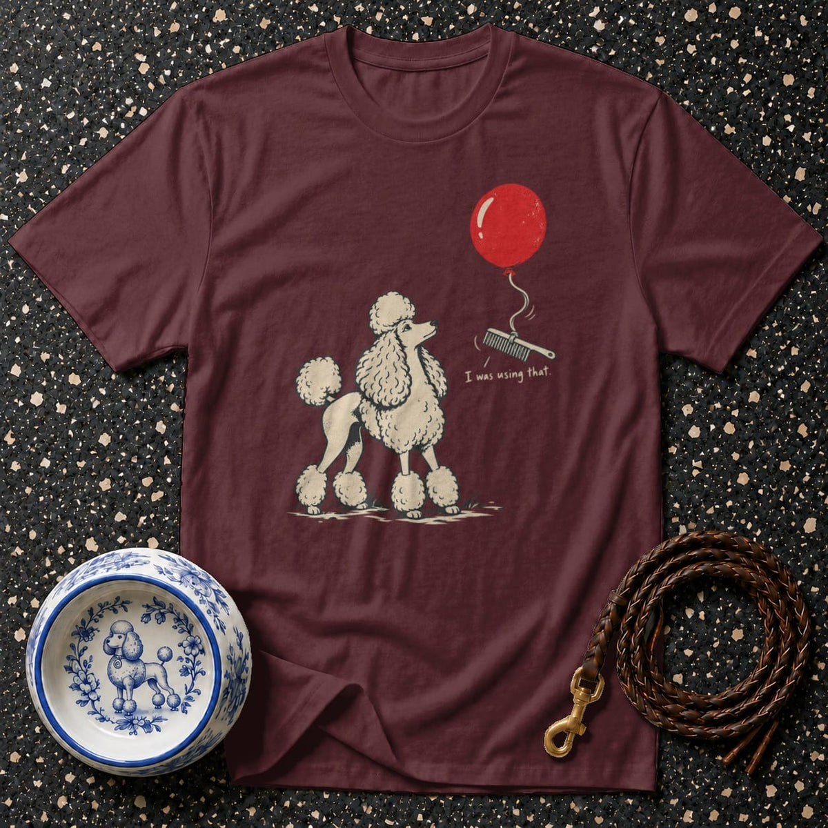 Maroon t-shirt with a poodle illustration, red balloon, and comb with text.