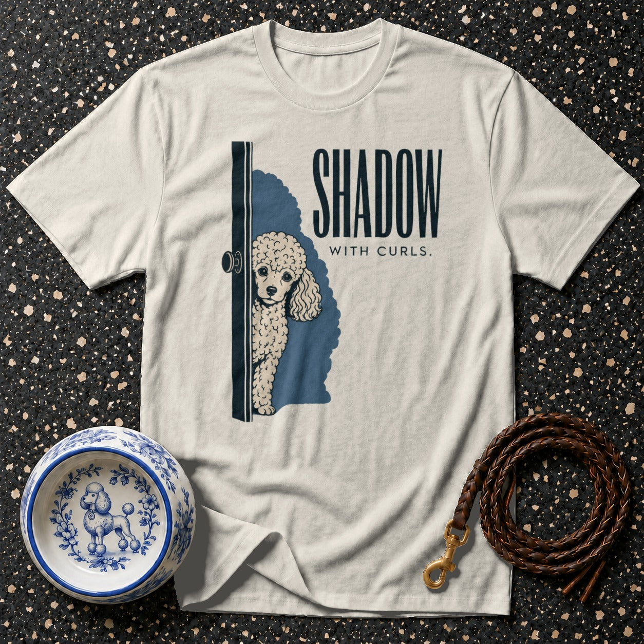 Cream t-shirt with a poodle peeking from behind a door and text "SHADOW WITH CURLS."