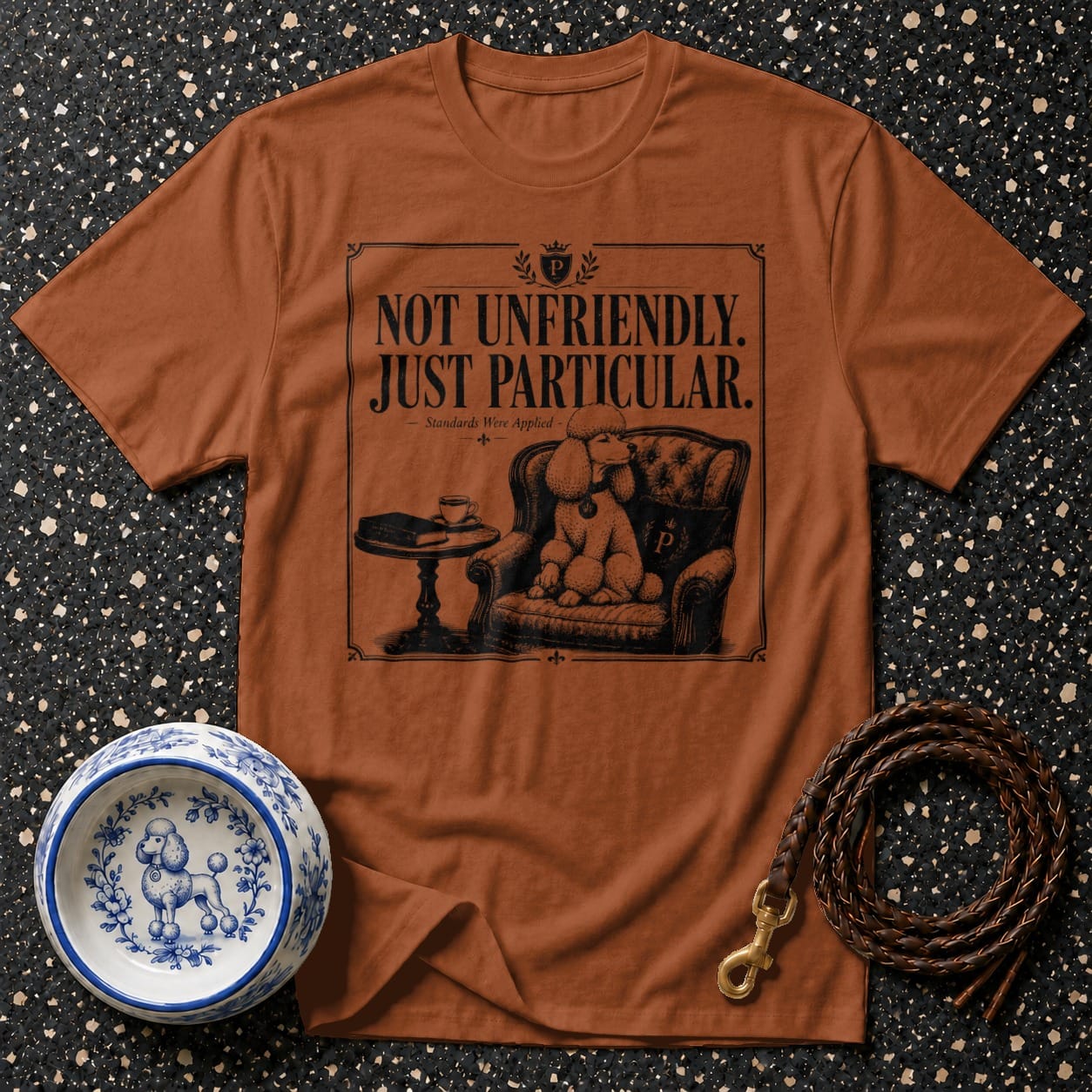 Brown t-shirt with black graphic: poodle in armchair, text "NOT UNFRIENDLY. JUST PARTICULAR."