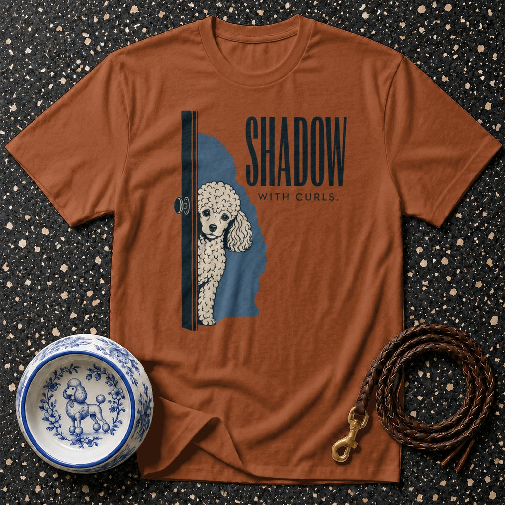 Orange t-shirt with a white poodle peeking from behind a door, text "SHADOW WITH CURLS."