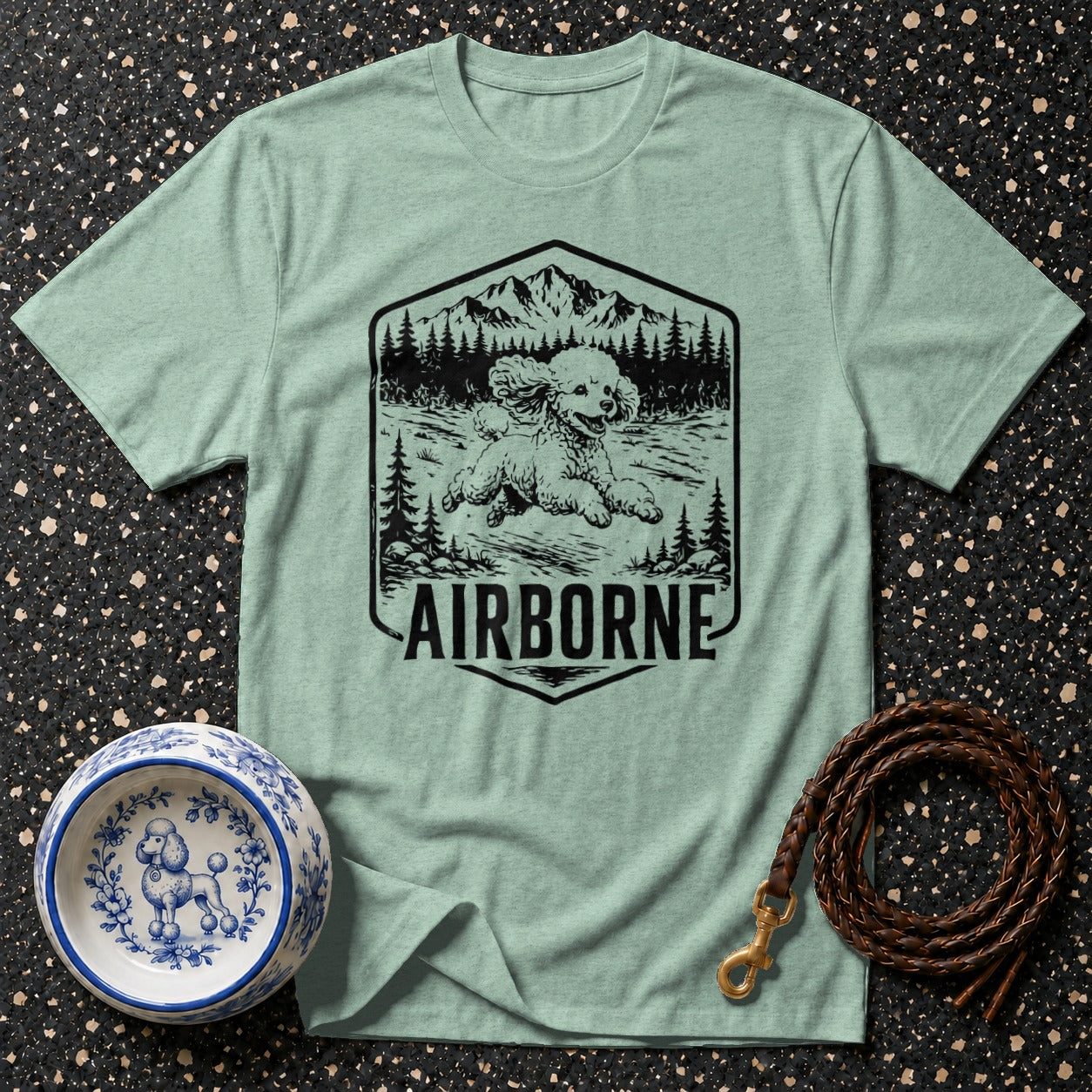 T-shirt with a graphic of a poodle running in a forest with mountains and the text "AIRBORNE."