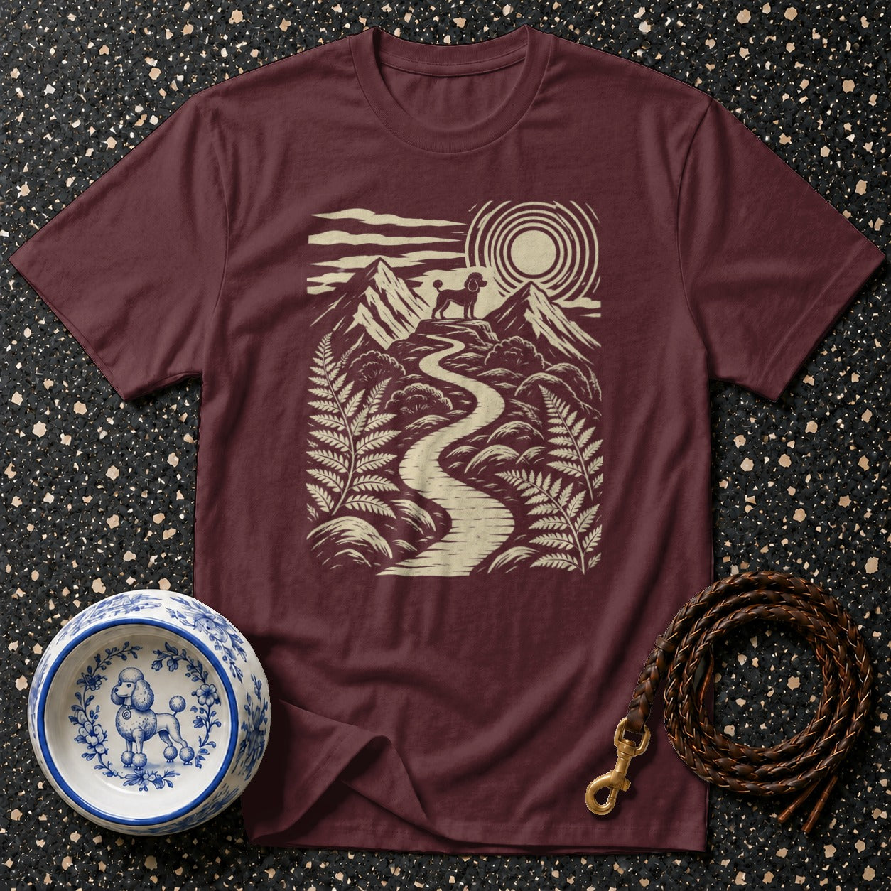 Maroon t-shirt with graphic of poodle on mountain path under sun.