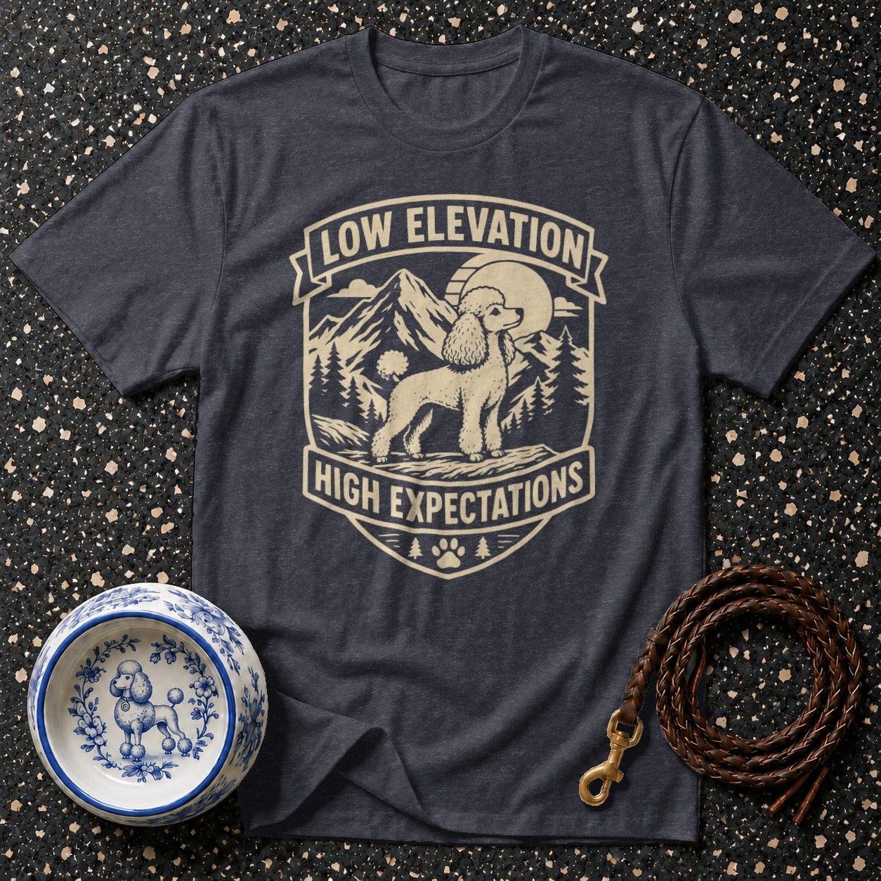 Dark t-shirt with a cream graphic of a poodle, mountains, and trees, text reads "Low Elevation High Expectations".