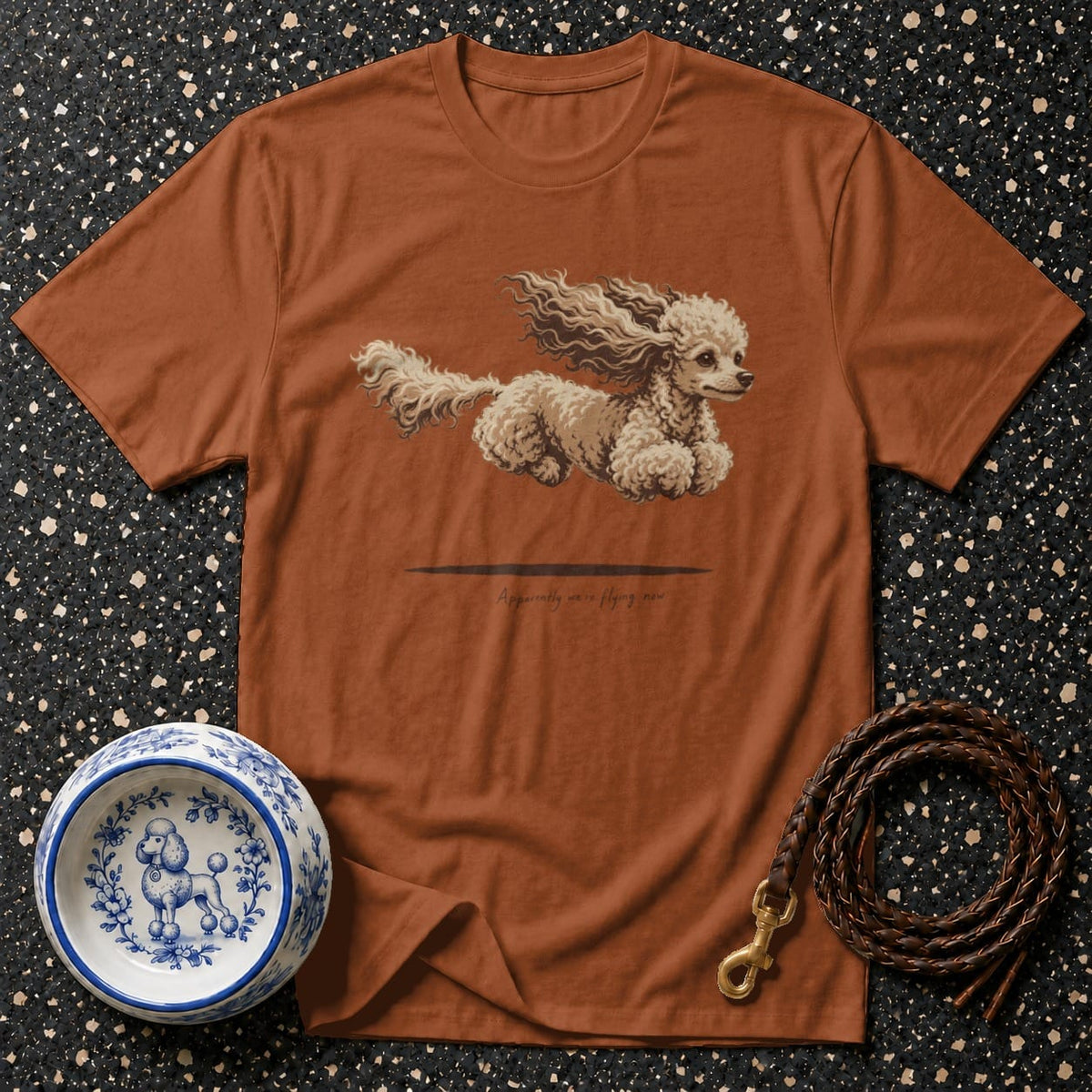 Brown t-shirt with a fluffy poodle illustration and text "Apparently we're flying now."