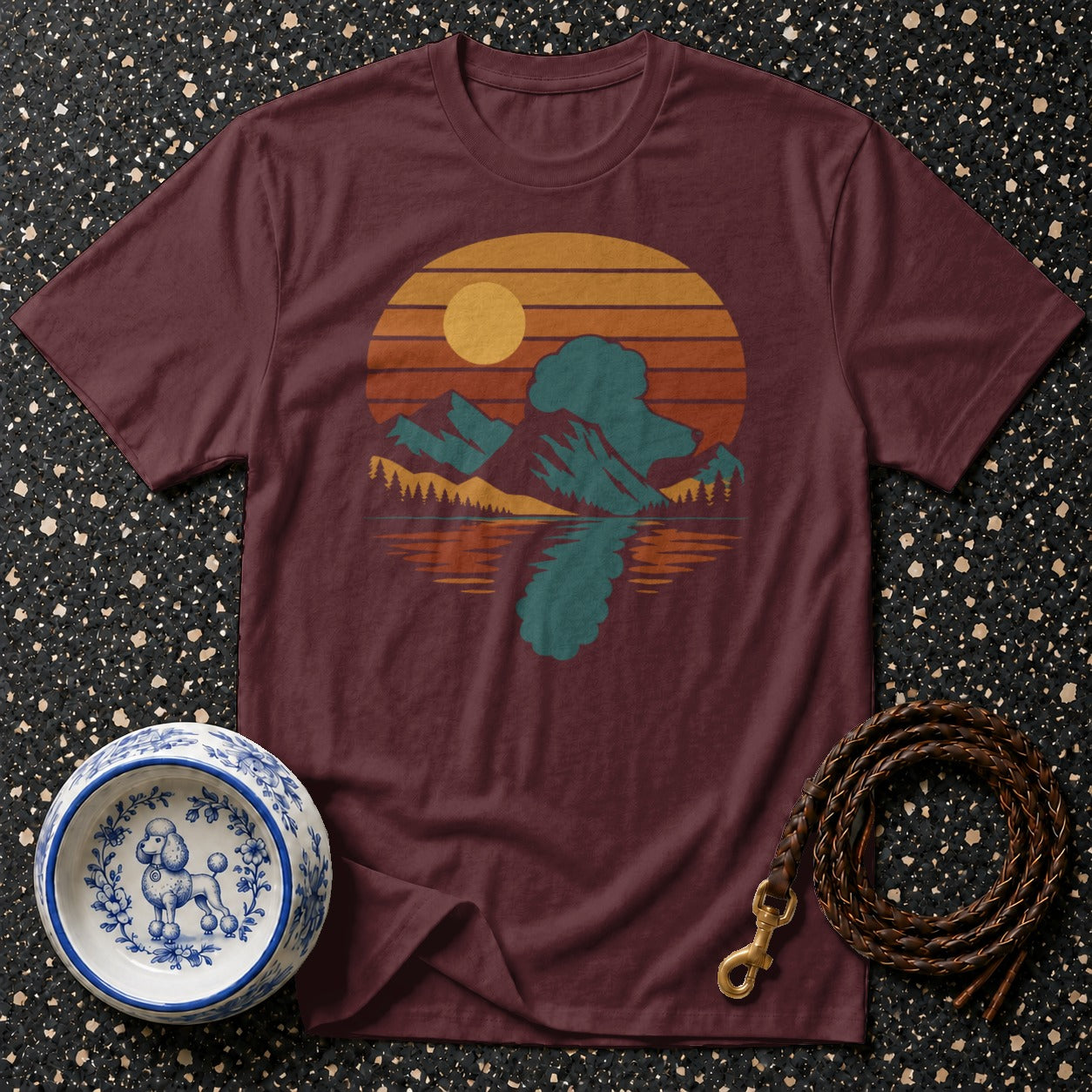 Maroon t-shirt with vintage mountain and lake sunset graphic, dog bowl, and leather leash.