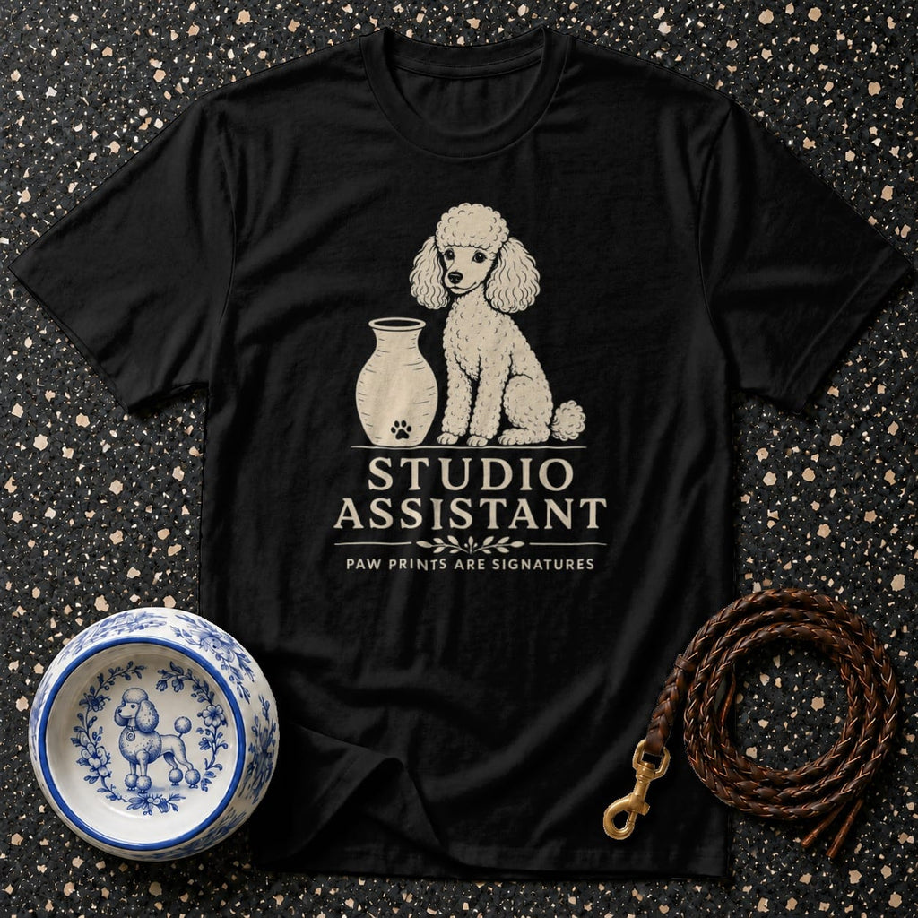 Black t-shirt with white poodle graphic, vase, and text "STUDIO ASSISTANT".