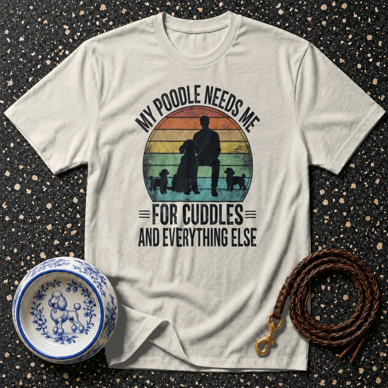 Light t-shirt with a graphic of a person and poodles with text "MY POODLE NEEDS ME FOR CUDDLES AND EVERYTHING ELSE".