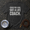 Dark grey t-shirt with white text "ASKED FOR A DOG. GOT A LIFE COACH."
