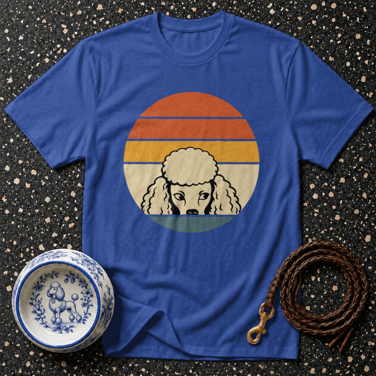 Blue t-shirt with vintage poodle graphic on sunset background, pet bowl, and leash.