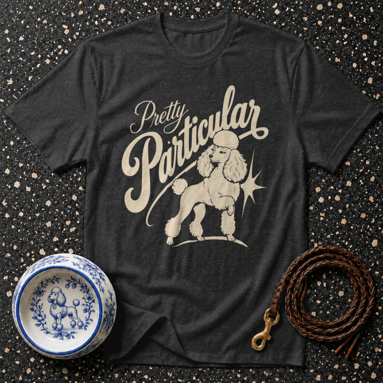 Dark t-shirt with "Pretty Particular" text and poodle graphic, plus a dog bowl and leash.
