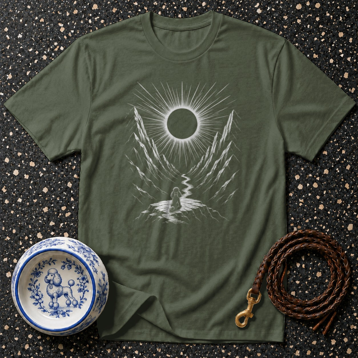 Green t-shirt with a white graphic of a person and dog at a mountain path under an eclipse.