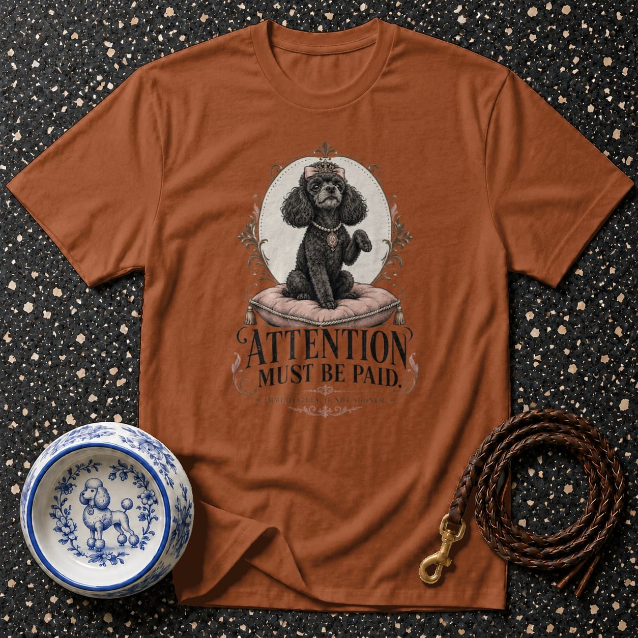 Brown t-shirt featuring a black poodle with crown and necklace, text "ATTENTION MUST BE PAID".