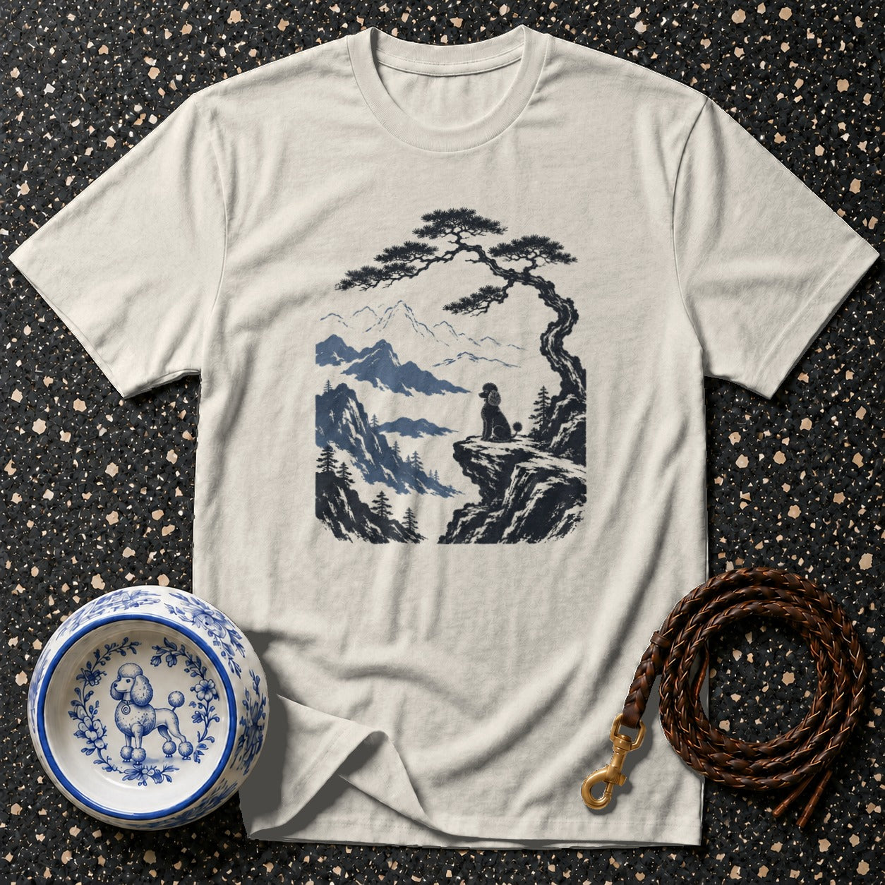 T-shirt with poodle on mountain cliff illustration, decorative bowl, and leather leash.