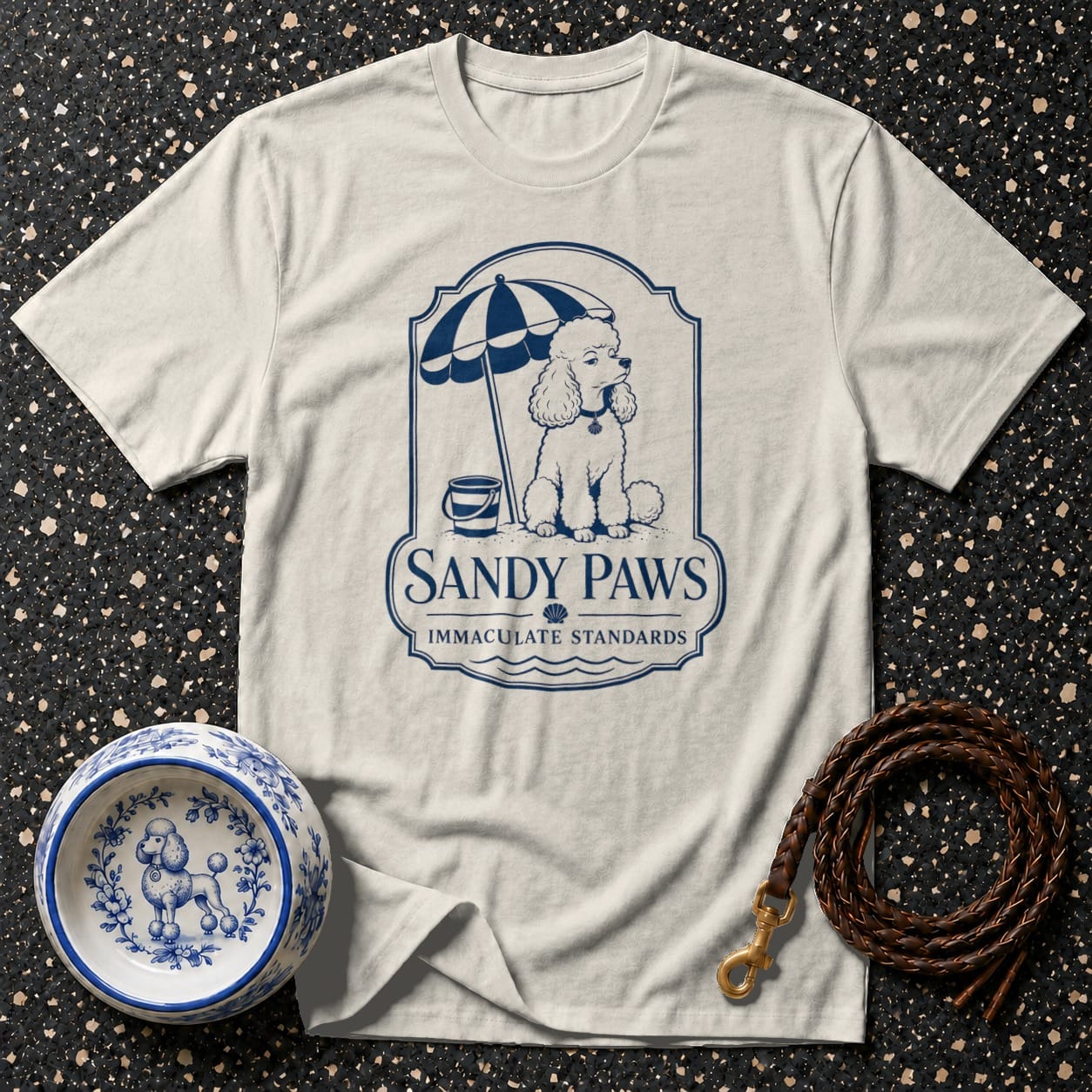 Cream t-shirt with Sandy Paws logo featuring a poodle under an umbrella on the beach.
