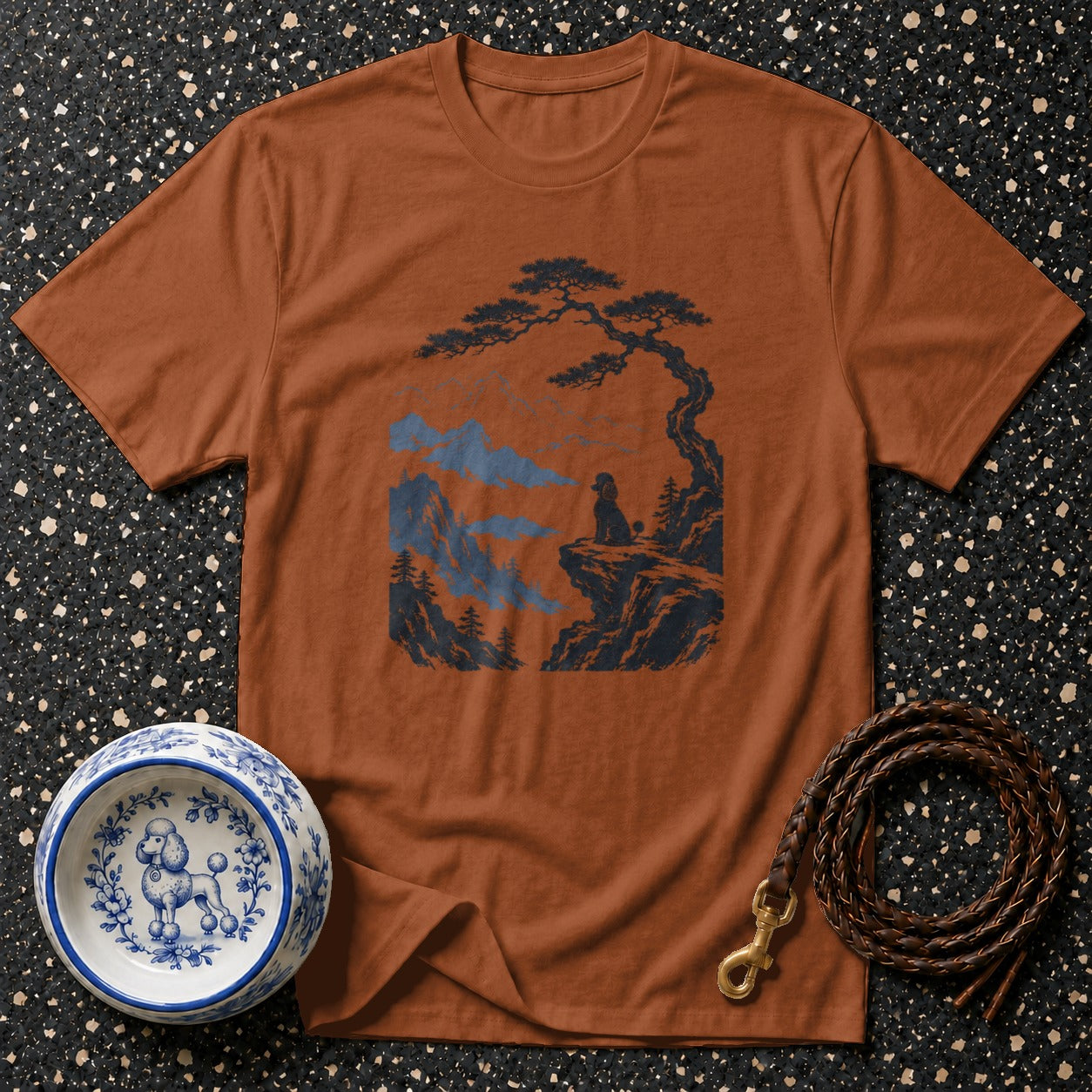 Brown t-shirt with a dark blue graphic of a dog on a cliff overlooking mountains.