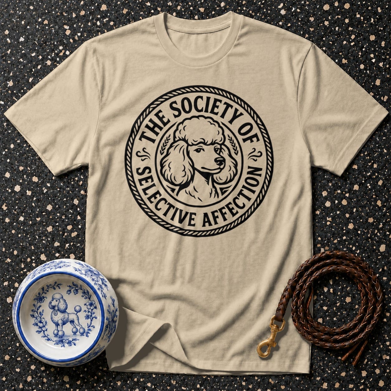 Tan t-shirt with a circular black design featuring a poodle head and text.