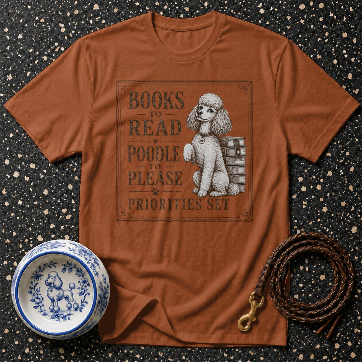 Brown t-shirt with illustration of poodle and text "Books to Read, Poodle to Please, Priorities Set".