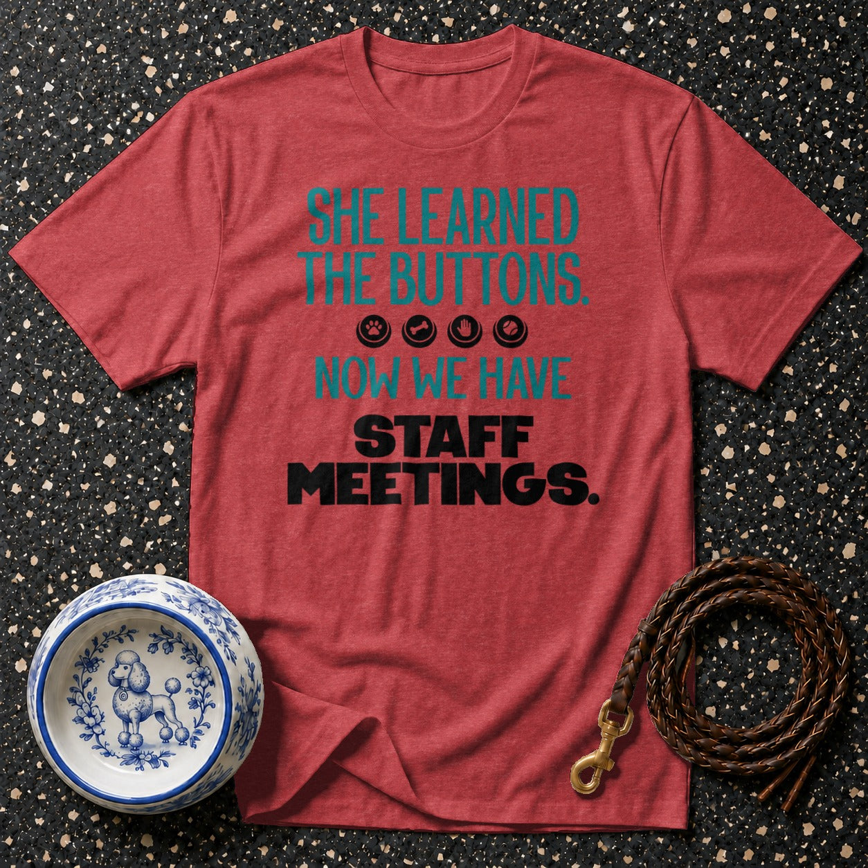 Red t-shirt with text "SHE LEARNED THE BUTTONS. NOW WE HAVE STAFF MEETINGS."