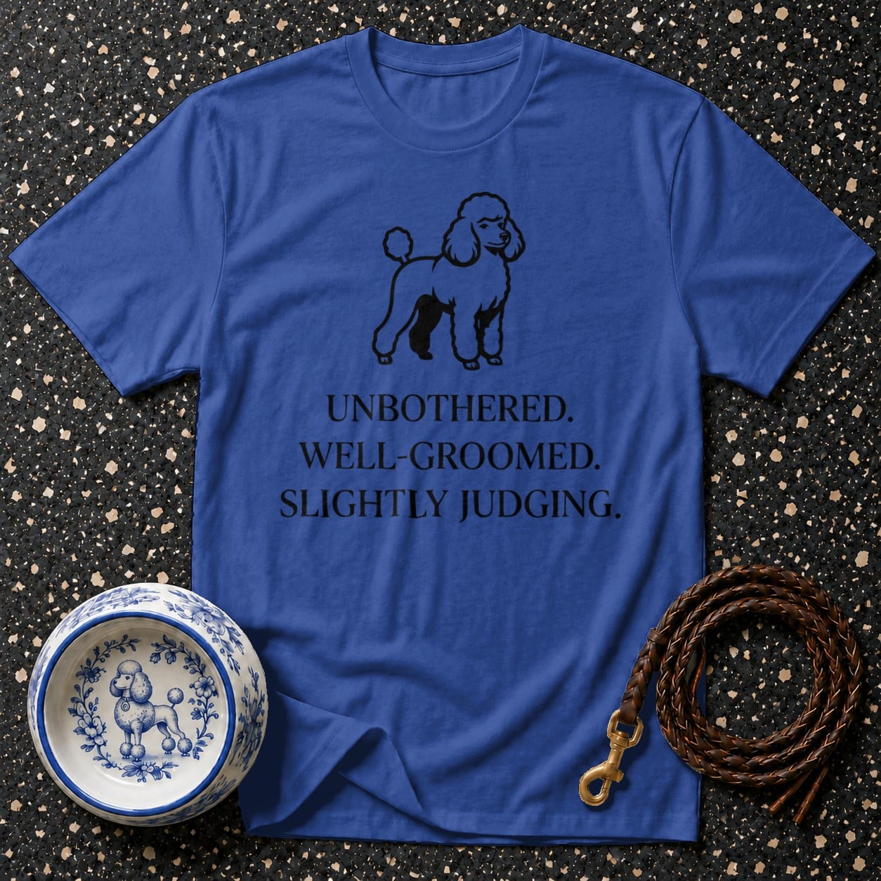 Blue t-shirt with black poodle graphic and text: UNBOTHERED. WELL-GROOMED. SLIGHTLY JUDGING.