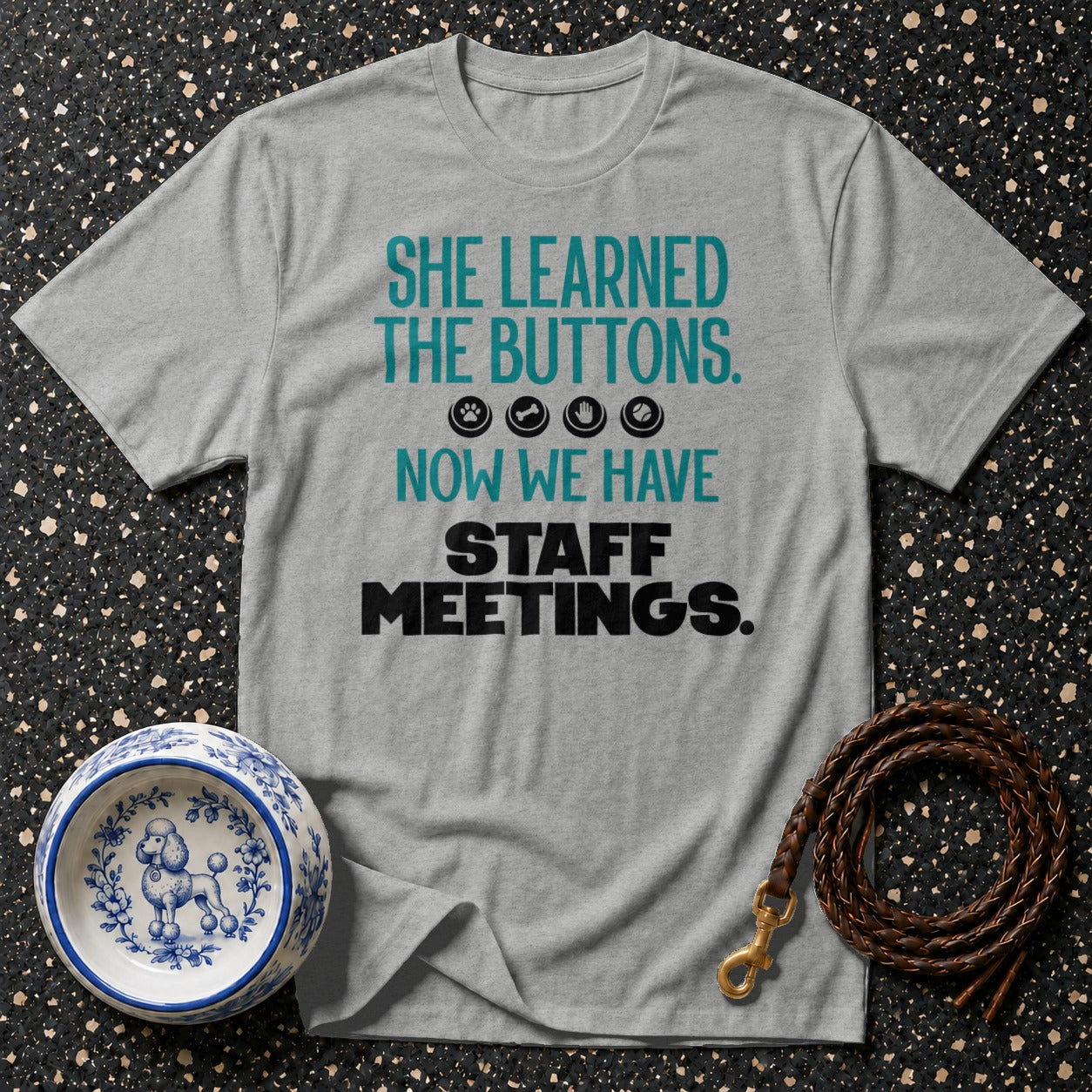 Grey t-shirt with text: "SHE LEARNED THE BUTTONS. ?�¾?¦´?Ž¾ NOW WE HAVE STAFF MEETINGS."