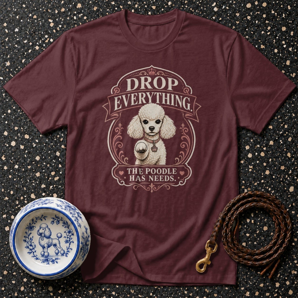 Maroon t-shirt with white poodle illustration and text "Drop Everything, The Poodle Has Needs".