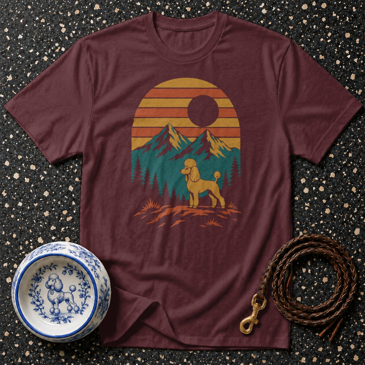 Maroon t-shirt with a yellow poodle graphic against a mountain sunset landscape.