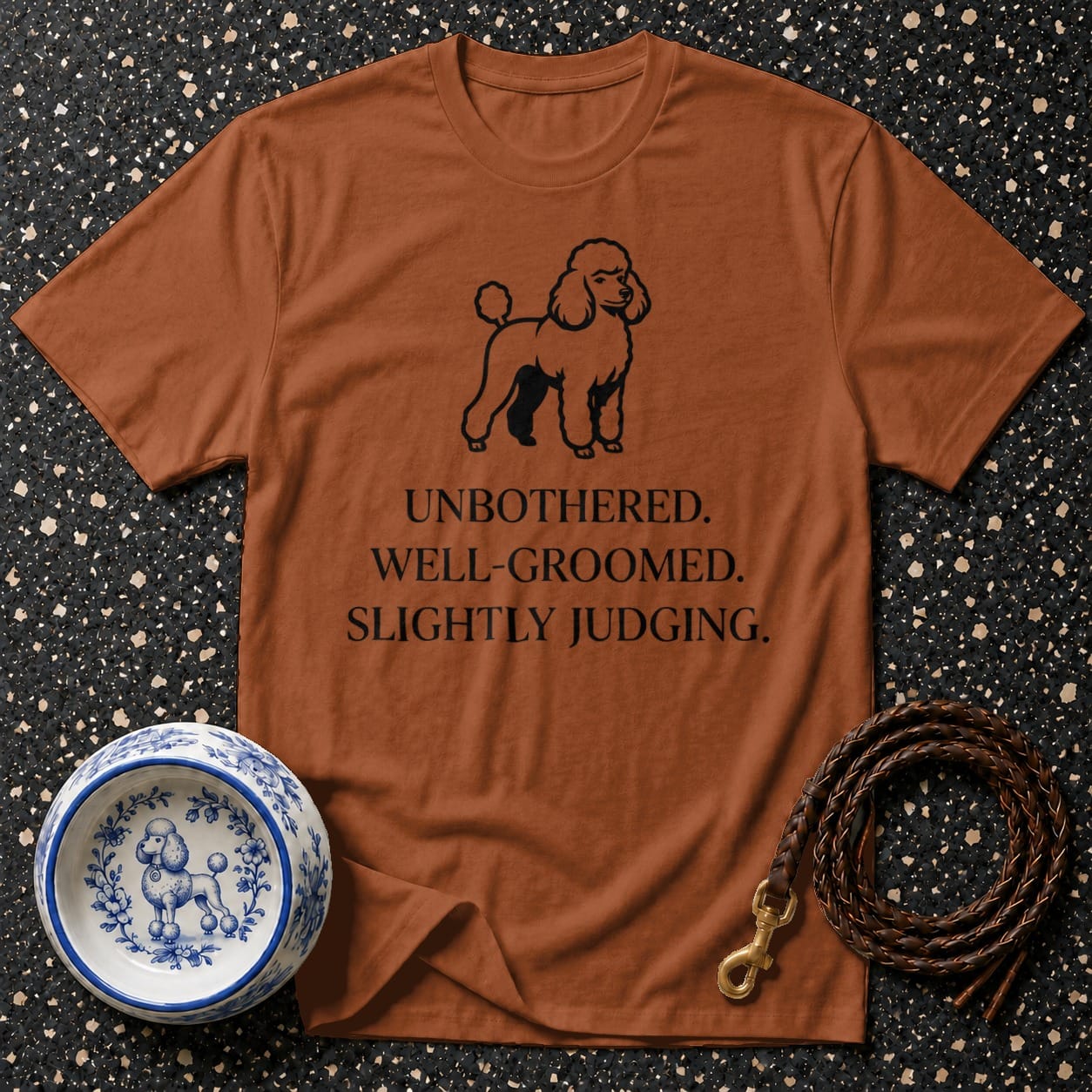Brown t-shirt with a poodle graphic and text "UNBOTHERED. WELL-GROOMED. SLIGHTLY JUDGING."