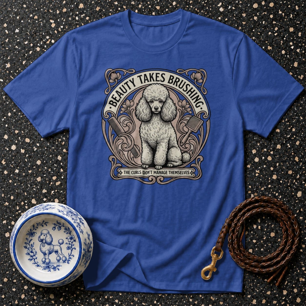 Blue t-shirt with poodle illustration and grooming text, next to dog bowl and leash.