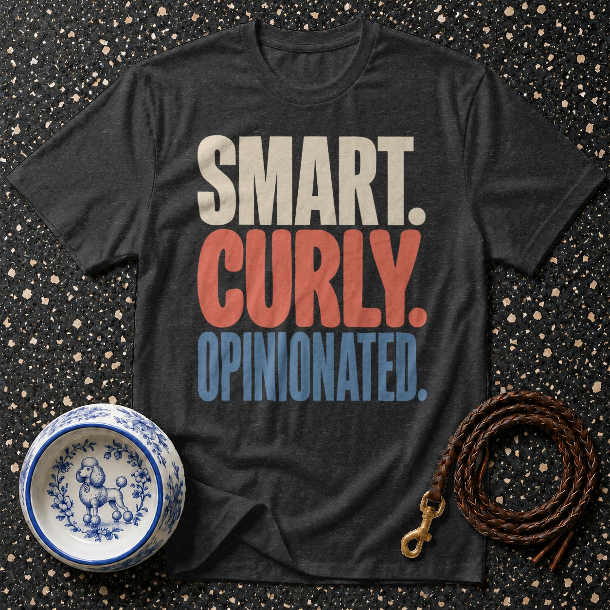 T-shirt with text "SMART. CURLY. OPINIONATED." next to a poodle-decorated bowl and leash.