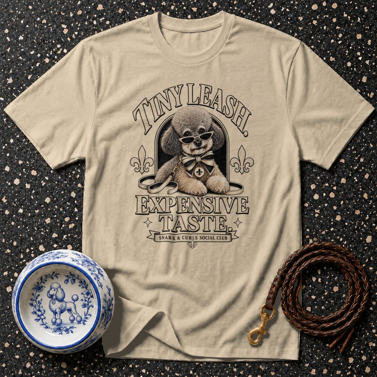 Beige t-shirt with a poodle wearing sunglasses and a bow tie, text "EXPENSIVE TASTE".